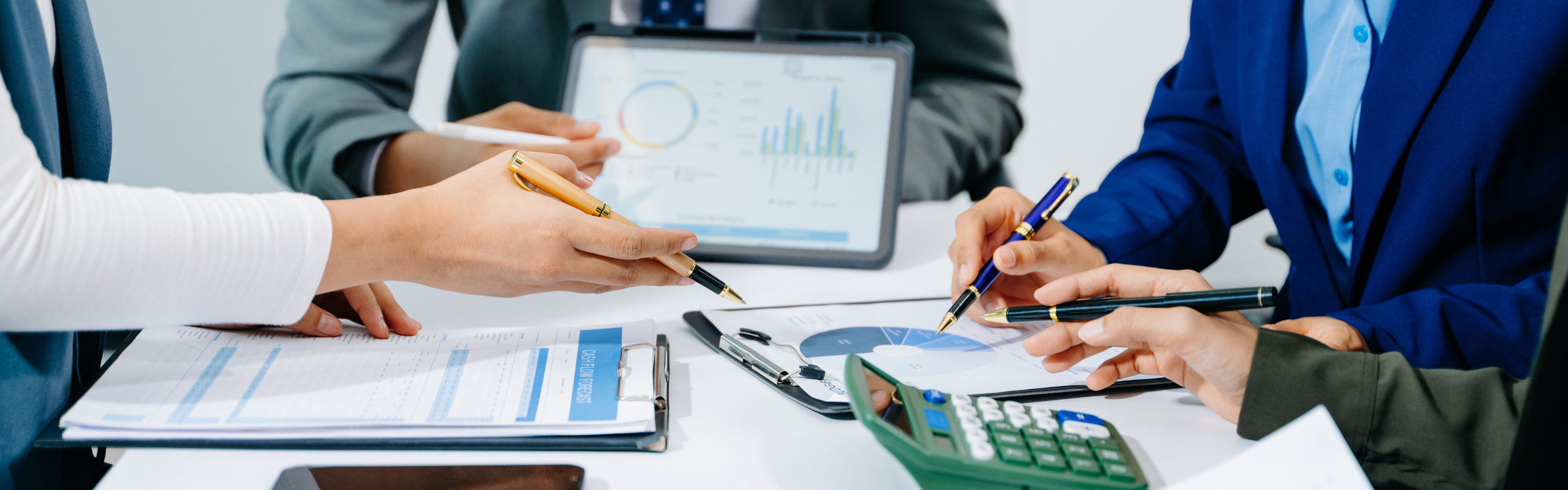 Grupa doradcza siedząca nad wykresami, w tle infografiki oraz kalkulator