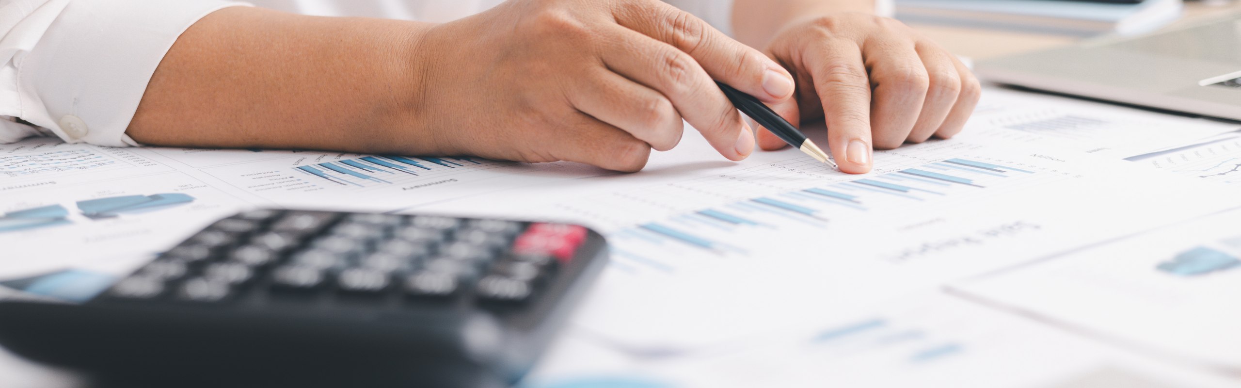 Businessperson using calculator and laptop with financial report on office desk, concept of accounting analysis, budget planning, data management and corporate finance strategy.