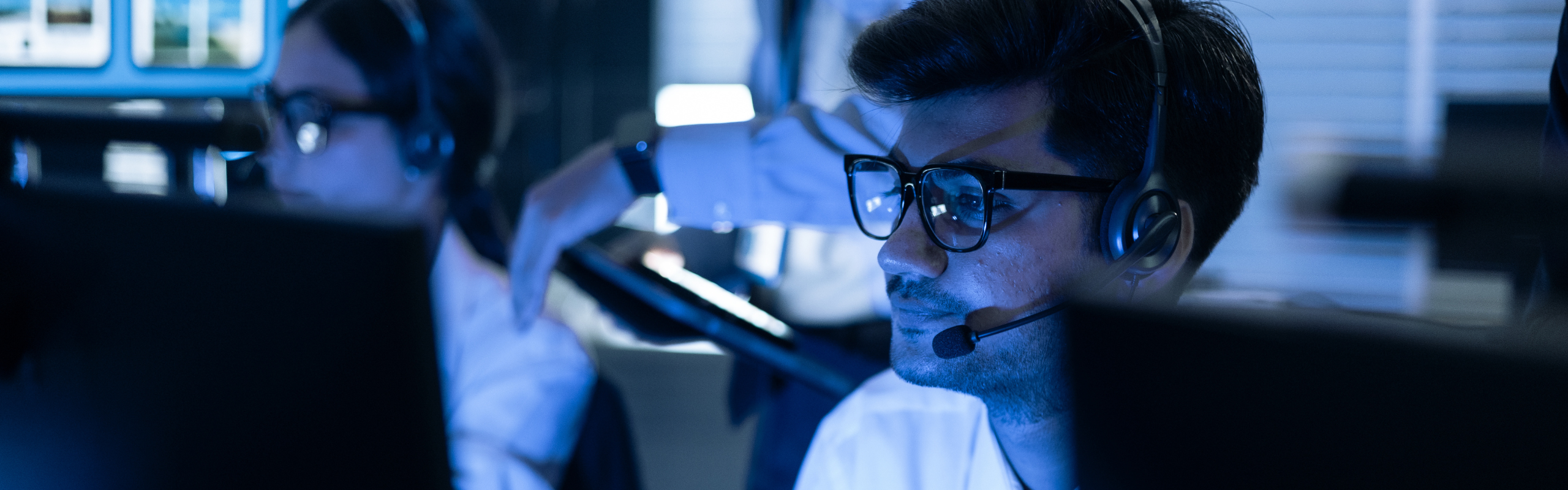 Focused male security operator with headset monitors data on screens in a high-tech control room